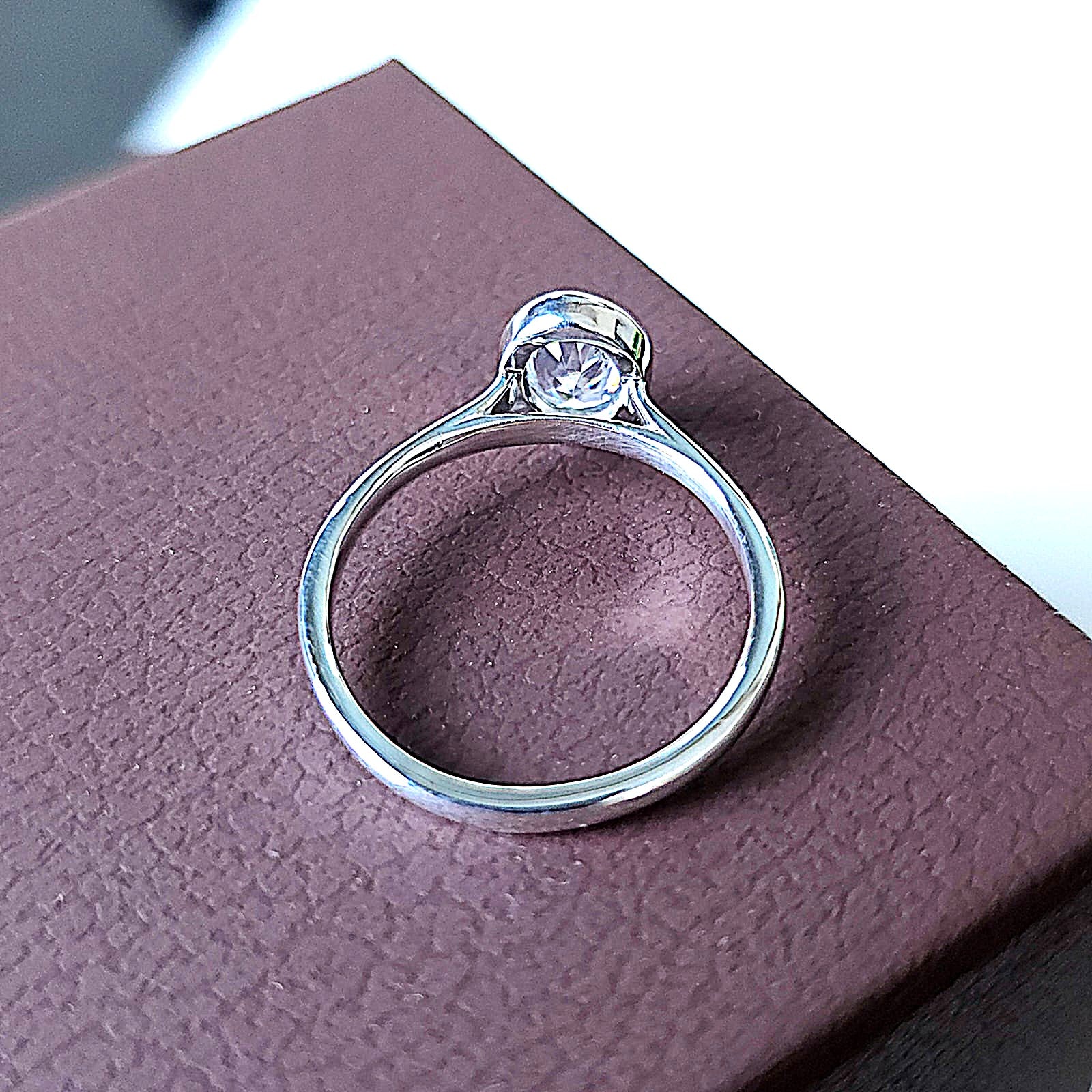 Overhead view of oval bezel engagement ring highlighting the full bezel setting and diamond facets.