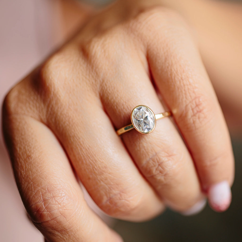 Model’s hand wearing the 1 ct oval bezel engagement ring against a neutral background.