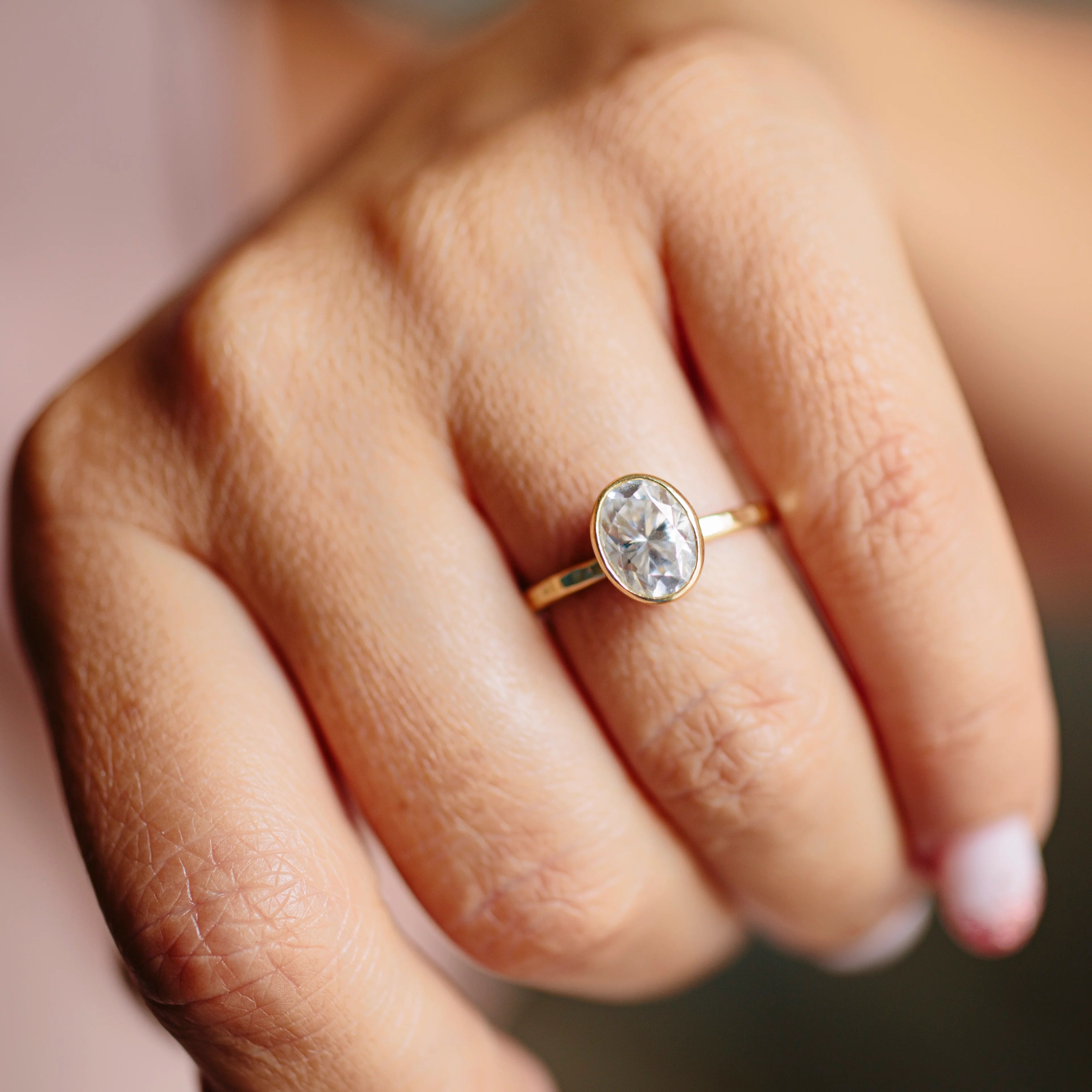 Model’s hand wearing the 1 ct oval bezel engagement ring against a neutral background.