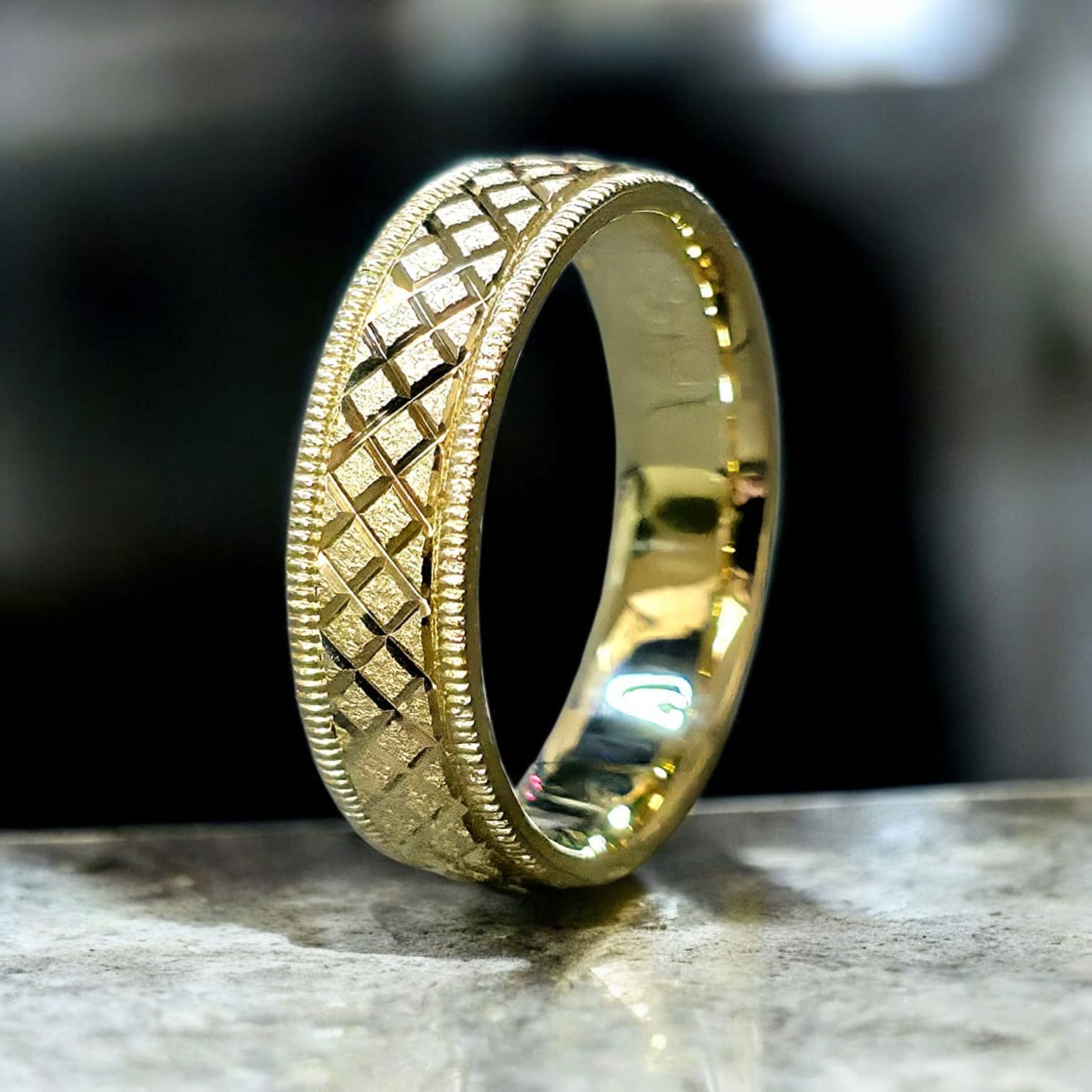 Crux cut gold wedding ring with milgrain edges standing view on stone background