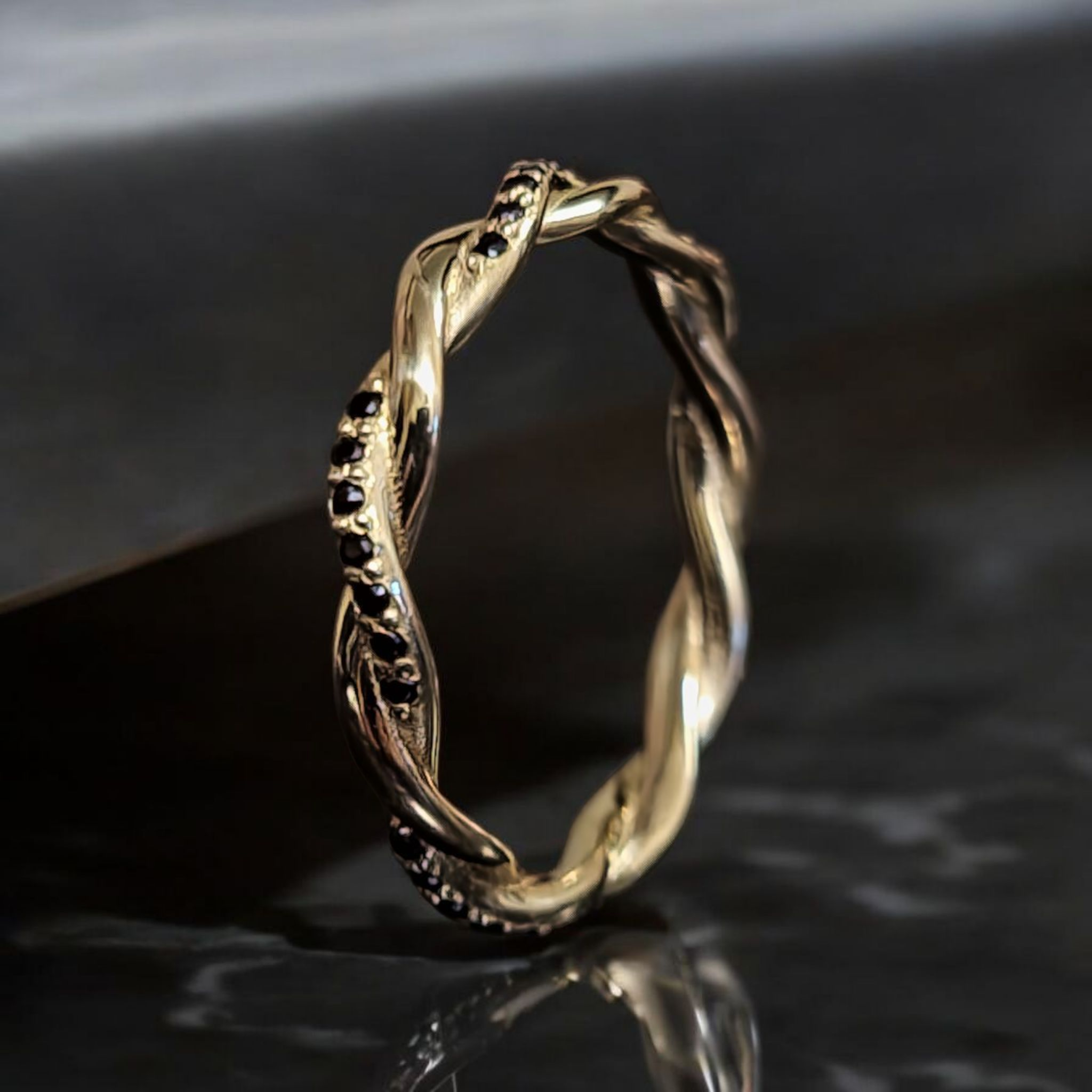 Twisted 14K yellow gold ring with black diamonds, standing view on dark background